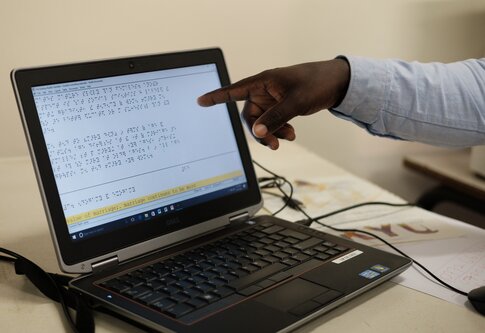 a hand pointing at a laptop screen displaying braille | © Light or the World