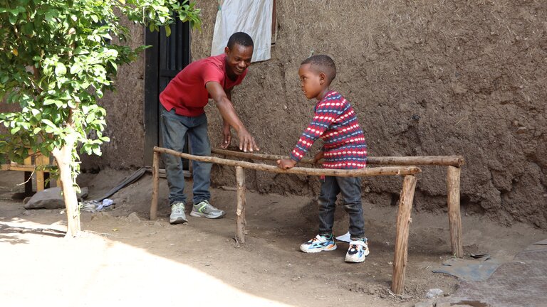 a person and child standing on a wooden railing | © Light for the World