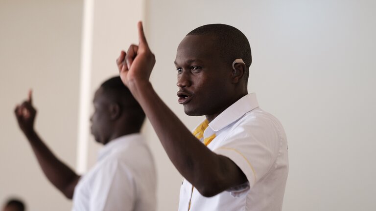 A man with a hearing aid in his ear raises his hand | © Light for the World 
